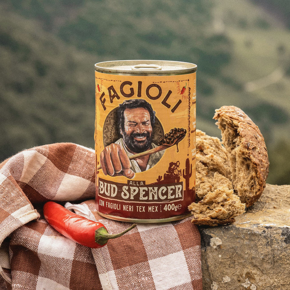 Can of Bud Spencer Beans with bread and chili pepper on a checkered cloth against a mountainous background